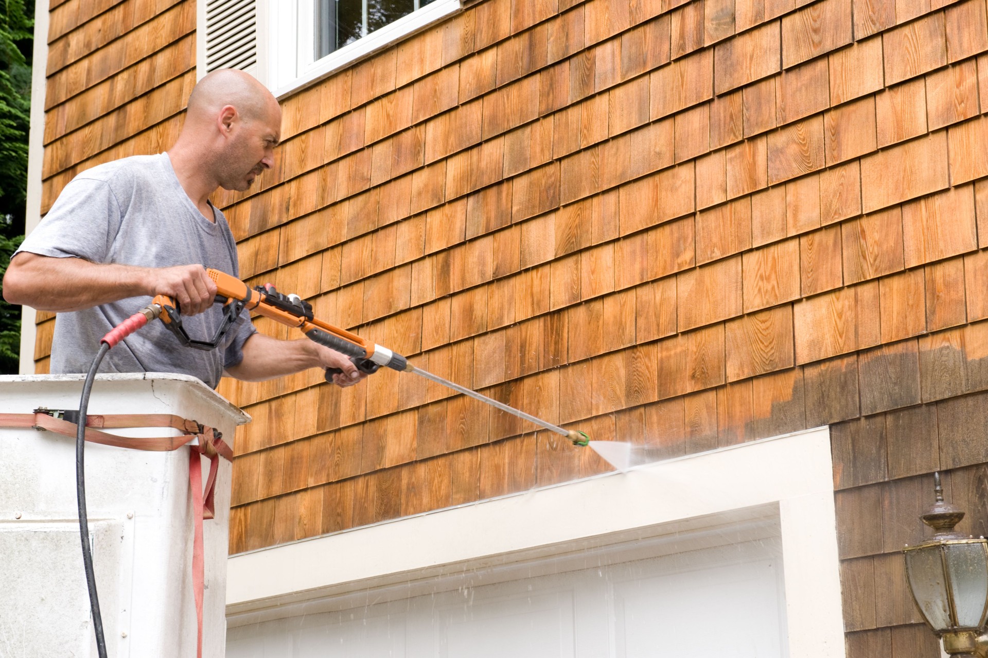 close up of man power washing exterior shingles